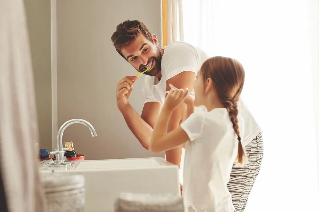 A parent and child brushing their teeth.