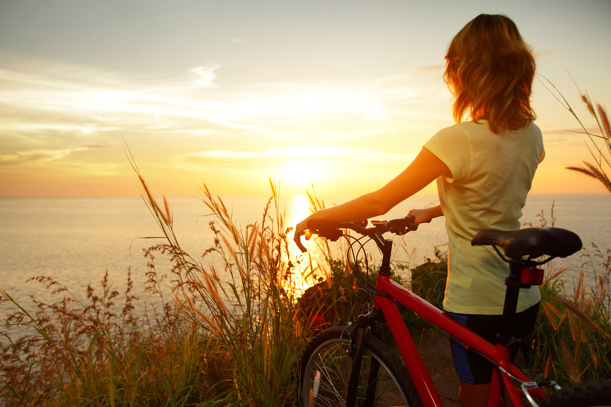 A woman standing with her bicycle at sunset.