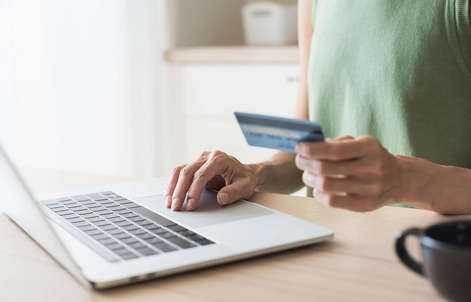 A person using a credit card beside a laptop.